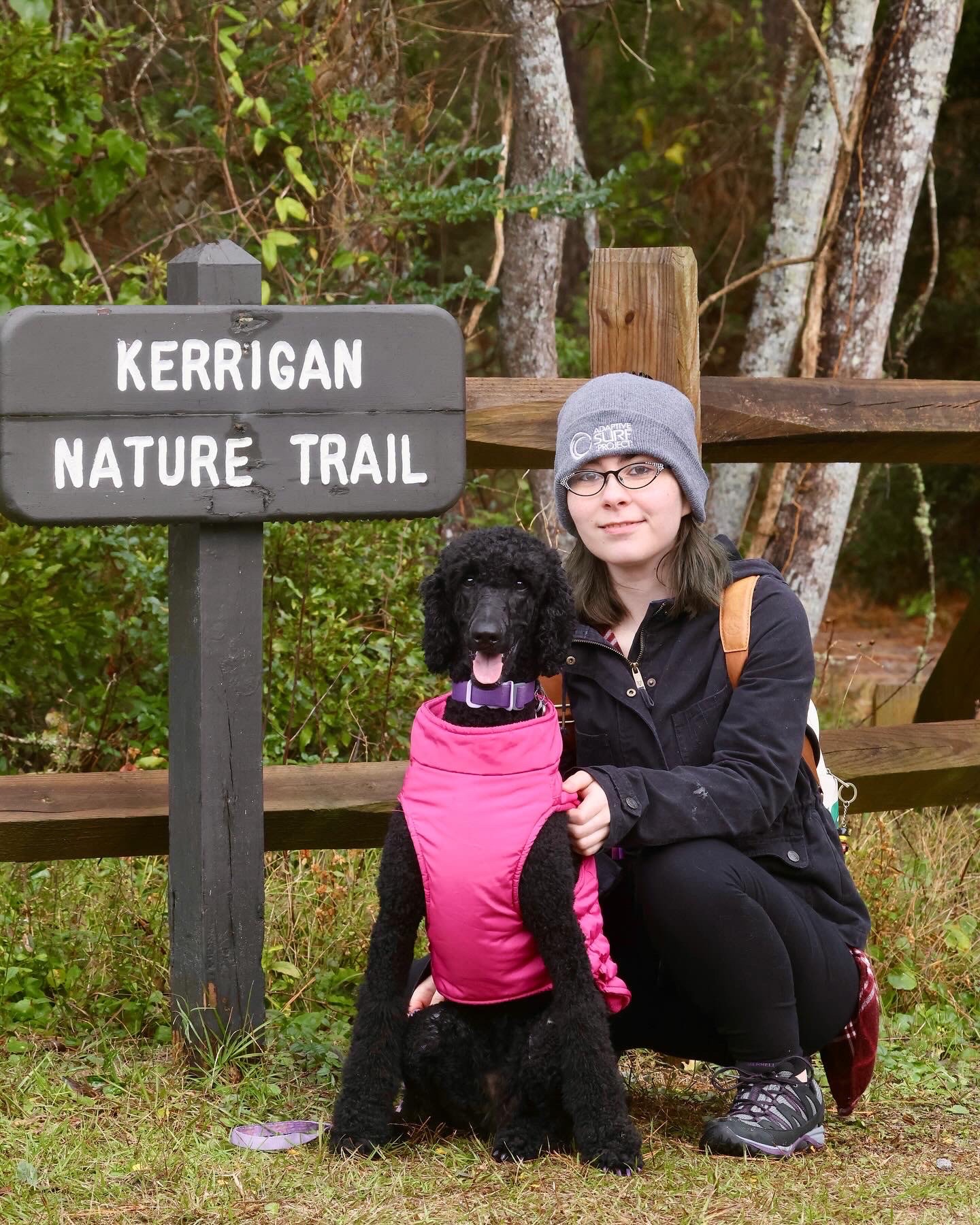 Eleanore and Jinkx, her black standard poodle, posing at a hiking trail entrance